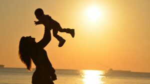Image of parent holding child up during sunset. If you're waiting on autism services, Norfolk Autism Center is here to help.